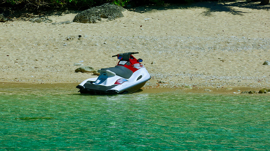 A jet ski is parked in the sea near the beach on the shore of a tropical island.