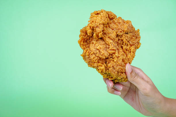istock Female hand holding fried chicken on green background. 2148963513