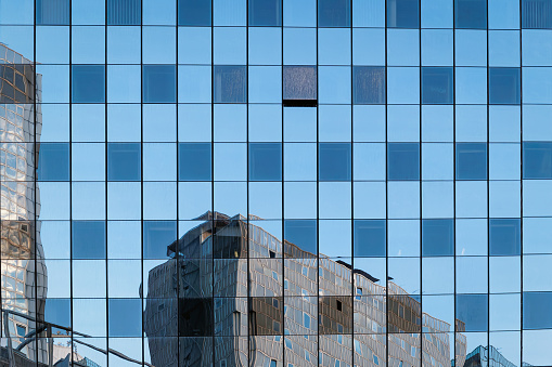 Facade of a skyscraper in which the surrounding buildings and blue sky are reflected.