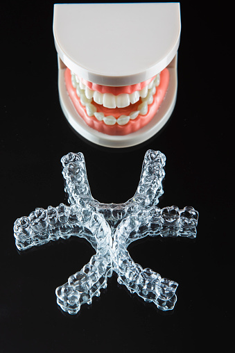 Close-up. Transparent aligners for artificial jaw teeth lie on a mirror on a black background