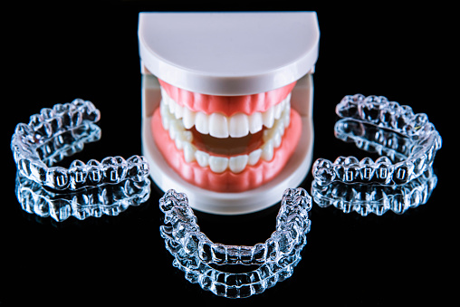 Close-up. Transparent aligners for artificial jaw teeth lie on a mirror on a black background