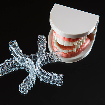 Close-up. Transparent aligners for artificial jaw teeth lie on a mirror on a black background