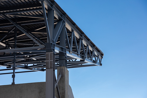 Fragment of a canopy. Metal beams on a concrete base support a metal roof against a blue sky