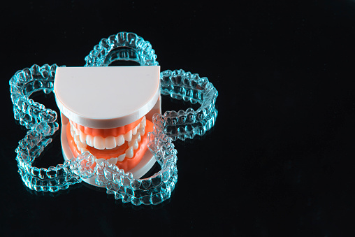 Close-up. Transparent aligners for artificial jaw teeth lie on a mirror on a black background