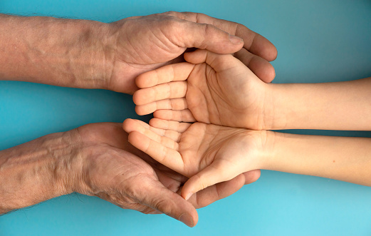 the hands of a child and the hands of an old man hold each other on a blue background. respect for generations in the family