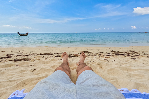 Young man's feet as he is lying on the beautiful sandy Ko Phangan beach on the Andaman sea in Thailand. His POV.