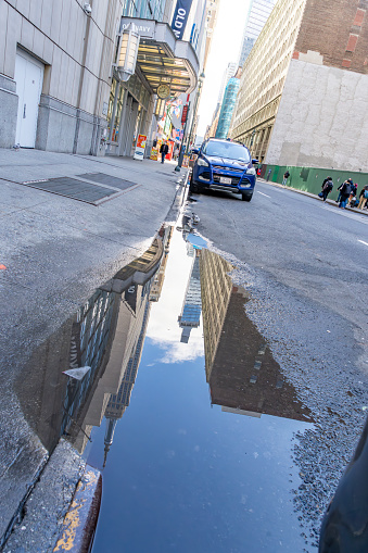 Seventh Avenue, Manhattan, New York, USA - March, 2024. Seventh Avenue near the Empire State Building, there is a rainwater puddle in the foreground with reflections of New York Buildings in it.