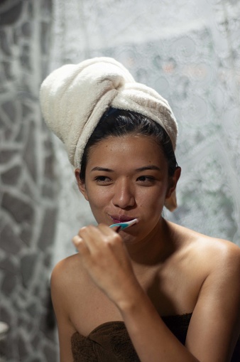 A young lady with a towel-wrapped head maintains oral hygiene by brushing her teeth, a daily ritual of self-care.