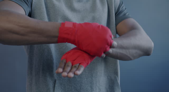 Close-up of male African American MMA fighter wrapping hands then hitting fists on purple color background