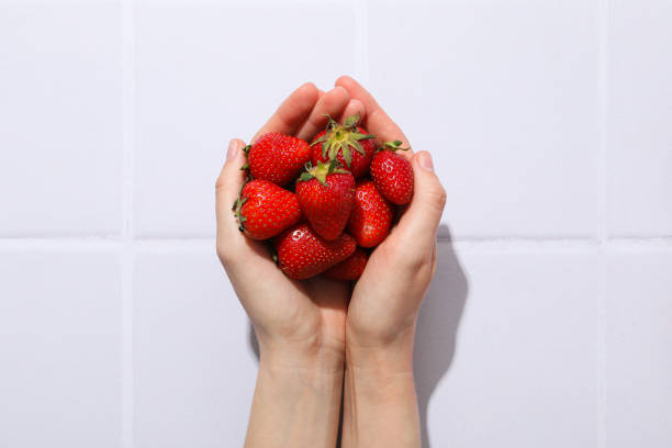 Caucasian female is showing bowl of strawberry to camera.
