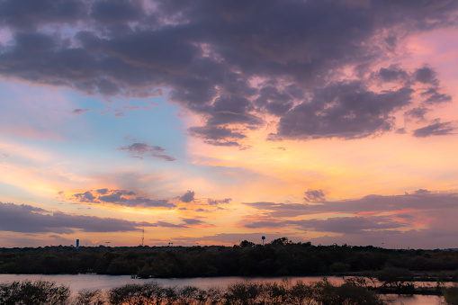 Dramatic colorful sunset clouds reflection along the treelined horizon  on Woodlawn Lake San Antonio Texas