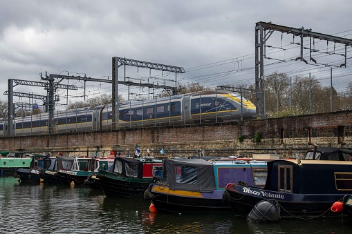 London, United Kingdom - April 03, 2024: Eurostar train passing by the boats of the St Pancras Bassin