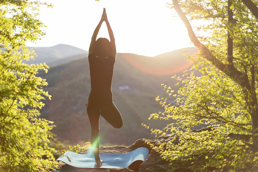 Mature woman doing yoga on top of a mountain, enjoying the the sunset and the tranquility of the beautiful surroundings.