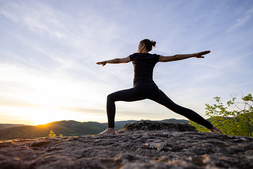 Mature woman doing yoga on top of a mountain, enjoying the sunset and the tranquility of the beautiful surroundings.