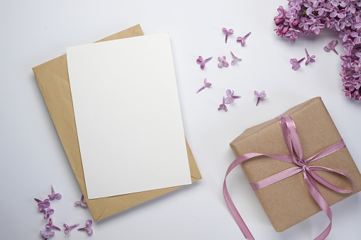 Composition with empty envelope and beautiful spring lilac flowers on a white background. Mockup card invitation greeting card postcard copy space template. Top view, flat lay. Space for text.