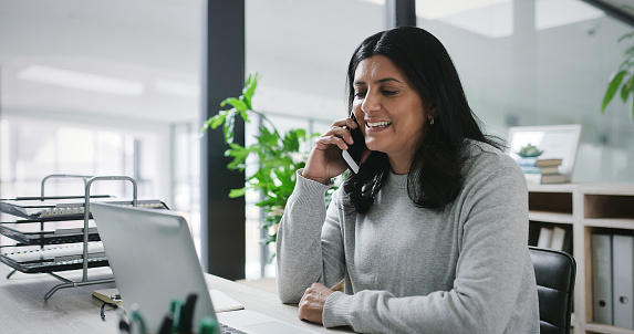 Laptop, phone call and smile with manager woman at desk in office for administration or communication. Computer, conversation and negotiation with happy mature boss at table in professional workplace