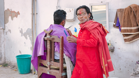 Indian barber shop - hairdresser cutting man's hair on streets of Jaipur city.