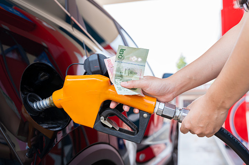 A person is filling up their car with gas and paying with cash. Concept of responsibility and practicality, as the person is using a traditional method of payment for a necessary expense.