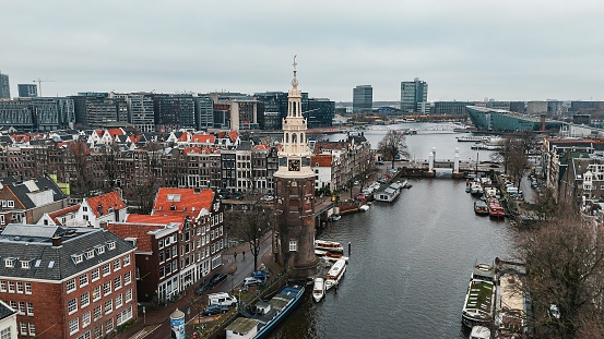 Aerial view of Montelbaanstoren Clock Tower in Amsterdam, Montelbaanstoren tower in Amsterdam, aerial city view of Montelbaanstoren Tower, aerial view of narrow canals of Amsterdam, popular place in Amsterdam\n\nThe Montelbaanstoren is a tower on bank of the Oudeschans – a canal in Amsterdam. The original tower was built in 1516 as part of the Walls of Amsterdam for the purpose of defending the city and the harbour. The top half, designed by Hendrick de Keyser, was extended to its current, decorative form in 1606. Since then the tower has been 48m tall.
