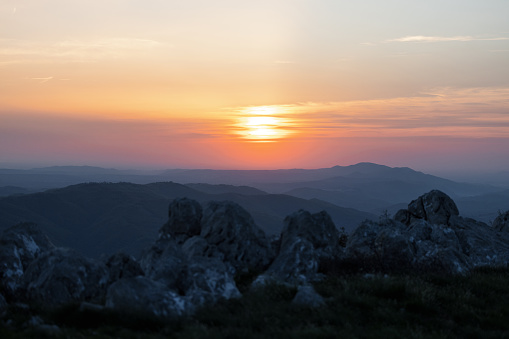 Vibrant sunset over a mountainous landscape, with silhouetted rocks in the foreground creating a serene scene.