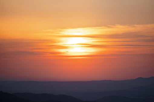 Vibrant orange sunrise over a hilly landscape, capturing the peaceful start of the day.