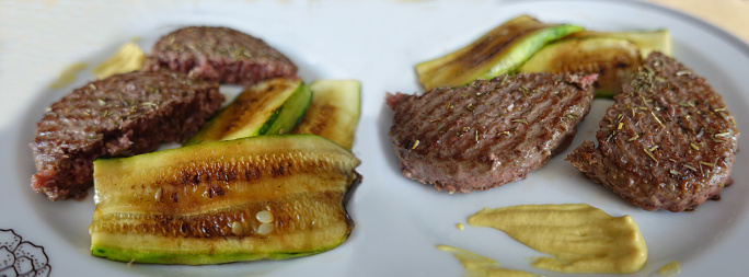 Browned ground beef garnished with Provence herbs served with barbecued slices of zucchini and mustard