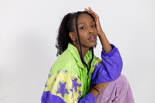 Close-up portrait shot of a young black woman posing in a studio in Newcastle Upon Tyne. She is wearing retro bright colourful clothing. She is looking at the camera with her hand on her head.

Videos are available similar to this scenario.