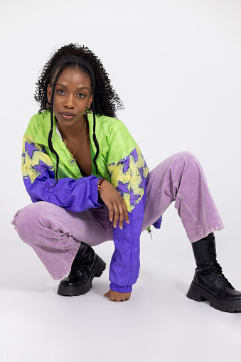 Medium portrait shot of a young black woman posing in a studio in Newcastle Upon Tyne. She is wearing retro bright colourful clothing. She is looking at the camera in a low squatting position.

Videos are available similar to this scenario.