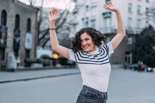 Shot of a cheerful woman with curly hair jumping in the city.