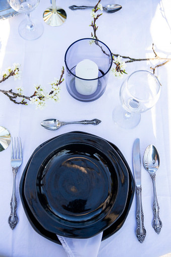 Black plates, glasses, candle, blossom branch and silverware for table setting. Vertical photo