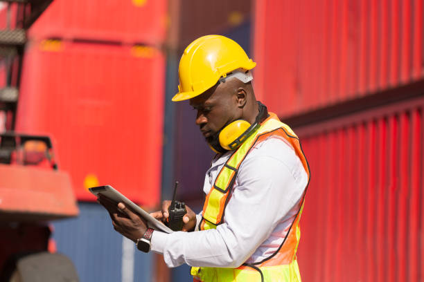 istock Male container yard worker loading containers box at commercial dock site. Male worker control loading container box from cargo freight ship for import export 2148983570