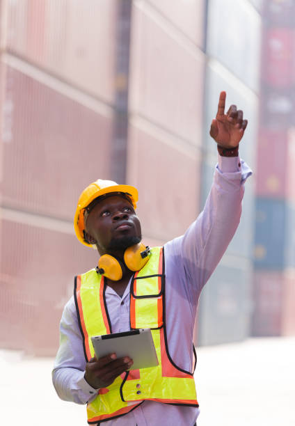 istock Male container yard worker loading containers box at commercial dock site. Male worker control loading container box from cargo freight ship for import export 2148983571