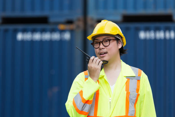 istock Male container yard worker loading containers box at commercial dock site. Male worker control loading container box from cargo freight ship for import export 2148983780