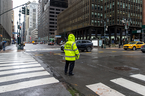 42nd Street, Manhattan, New York, USA - March, 2024. NYPD Traffic Officer on duty at a crossroads in Manhattan in a rain shower on Third Avenue and East 42nd Street Crossroads.