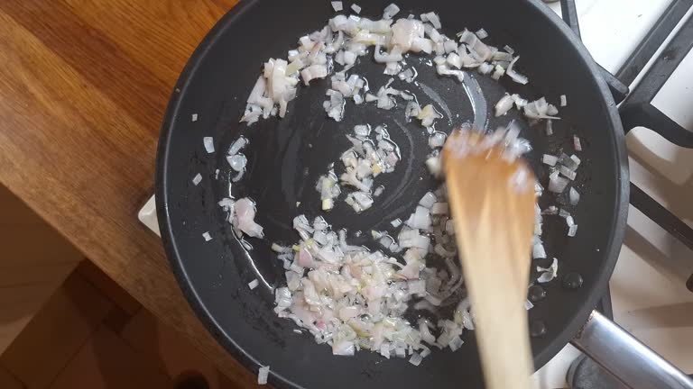 Stir in finely chopped onions. Diced onions in a pan. Finely chopped onions stirred with a wooden spatula. Concept of home cooking, culinary and gastronomy.