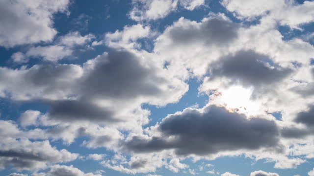 Blue sky with white clouds. Sun rays emerge through the clouds. Puffy fluffy white clouds. Cumulus clouds cloudscape timelapse. Summer blue sky time lapse.