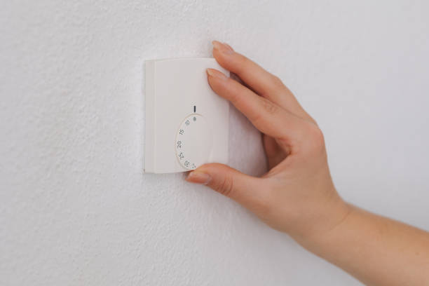 istock Side view of human hand turns off the heating at home. Central Heating thermostat control dial adjustment 2148992100