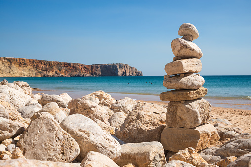 Zen-inspired stacked stones against a scenic seascape at Lagos beach in the Algarve, Portugal. A serene view with clear blue skies and golden sands.