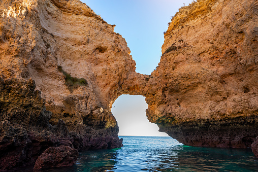 A breathtaking scene showcasing a natural arch framing the rugged cliffs of Lagos in the Algarve, Portugal. The clear blue sky and ocean complete this picturesque view.