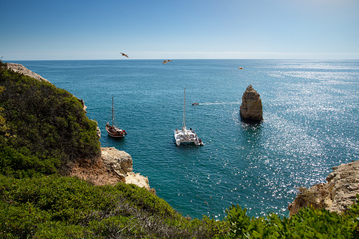 Stunning panoramic view of the ocean in Lagos, Algarve, featuring sailboats, a rocky coastline, and clear blue skies. Perfect for a peaceful day out.