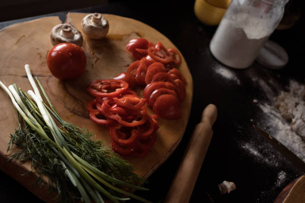 ingredients for baking pizza on dark table: tomatoes, mushrooms, red sweet pepper, rye dough, flour and rolling pin