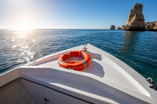 Experience the tranquility of a sunny day on a boat in Lagos, Algarve, Portugal with a scenic view of sparkling water and towering rocky cliffs.