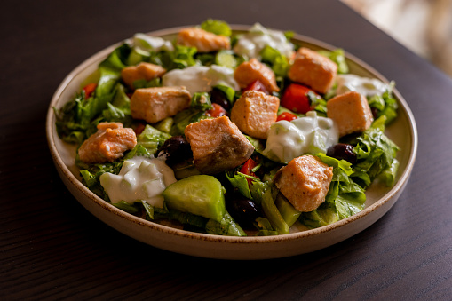 Close-up of a delicious Mediterranean salad featuring pieces of salmon fillet and a dollop of tzatziki sauce, offering a fresh and flavorful dining experience