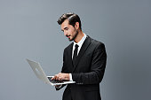Man business looks into laptop and works thoughtfully online via internet in business suit video call business talks on gray background copy place