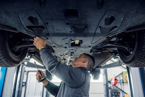 An auto mechanic is repairing car while standing under it at mechanic's shop. A car workshop worker is fixing car while standing under it at mechanic's shop. mechanic working under car stock pictures, royalty-free photos & images