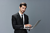 Man business looks into laptop and works thoughtfully online via internet in business suit video call business talks on gray background copy place