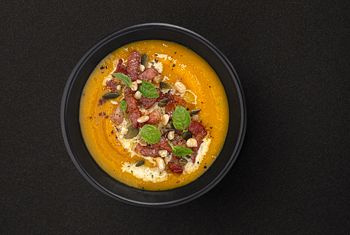 Pumpkin cream soup with pumpkin seeds and crispy bacon on black background with copy space, top view, package design element