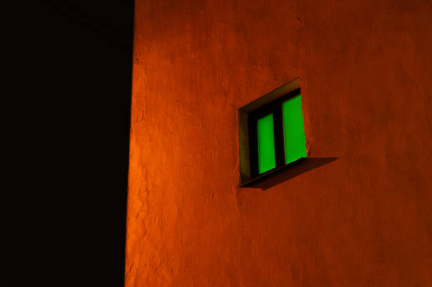 A window with a green tint is shown against a brick wall. The window is open, and the light coming through it casts a green shadow on the wall