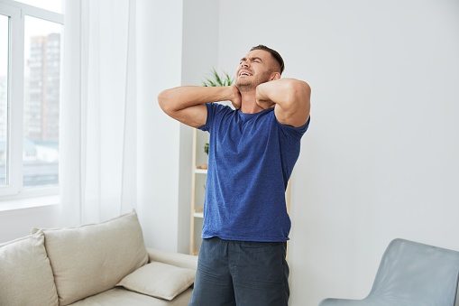 Man back neck and shoulder pain, inflammation of muscles and ligaments rupture during sports, inflammation and injury, in a blue t-shirt at home. High quality photo