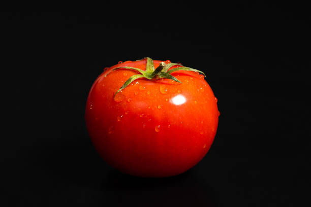 Ripe red tomato on a black background close-up. Organic food.